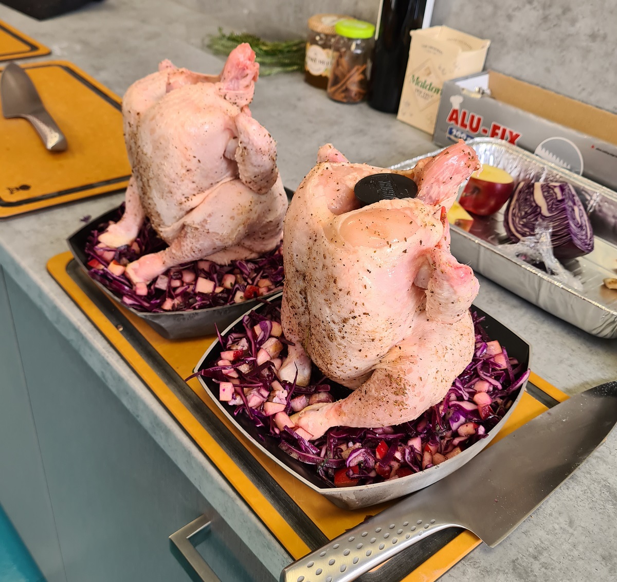 Pripravené dve celé kurčatá na stojanoch na hydinu Weber Deluxe s červenou kapustou v miskách